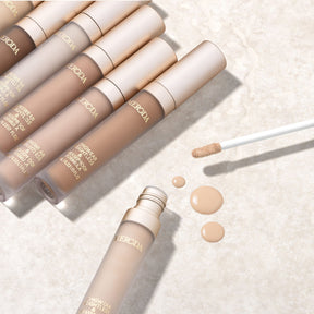 Universal Concealer in diverse shades with a creamy liquid texture and applicator on a light stone background.
