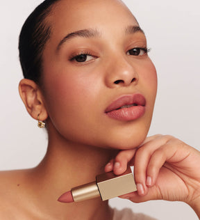 Velvet Dream Lipstick in Perfect Nude held by a model, featuring a soft matte finish and natural mauve color.