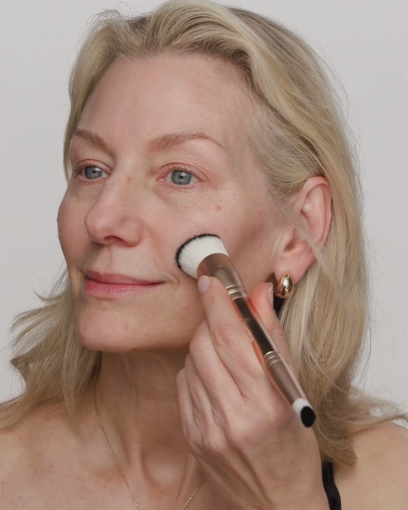 Mature woman blends Changing Foundation with a 2-in-1 Build & Conceal Brush for a natural finish.