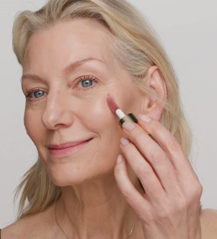 Model applying Mini Liquid Blush in Dusty Rose on cheeks using a makeup brush for a natural look.