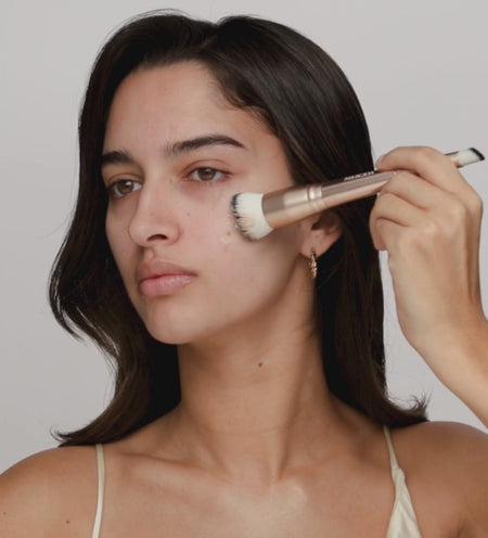 A model applying the shade-adapting foundation smoothly onto her face using a dual-ended makeup brush.