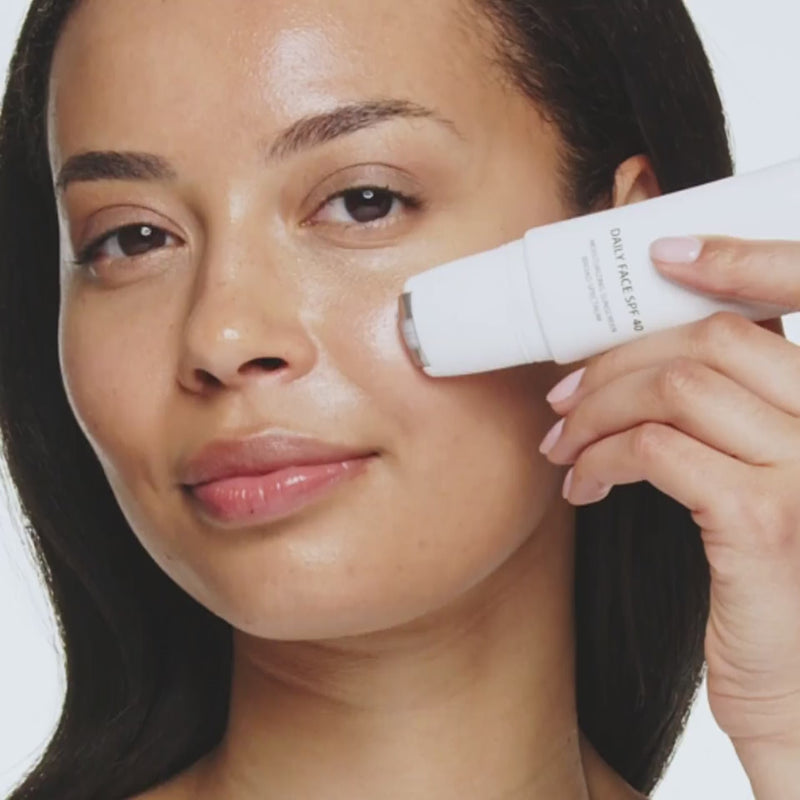 Daily Face SPF 40 applied with a cooling metal rollerball to a woman's cheek for a hydrated, glowing finish.