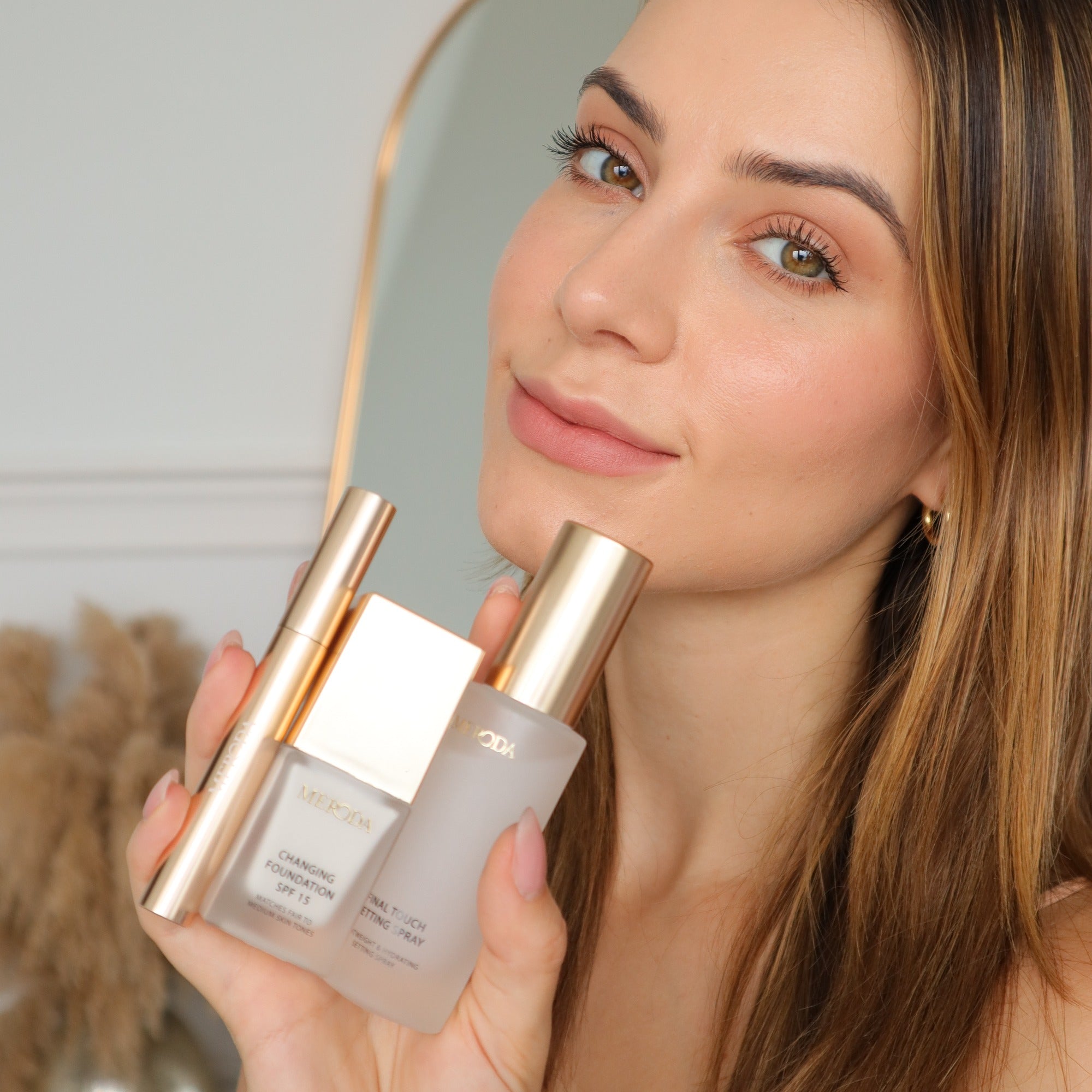 Woman holding Meroda Cosmetics Travel Kit with mini Changing Foundation, Final Touch Setting Spray and Gilded Lashes Mascara.