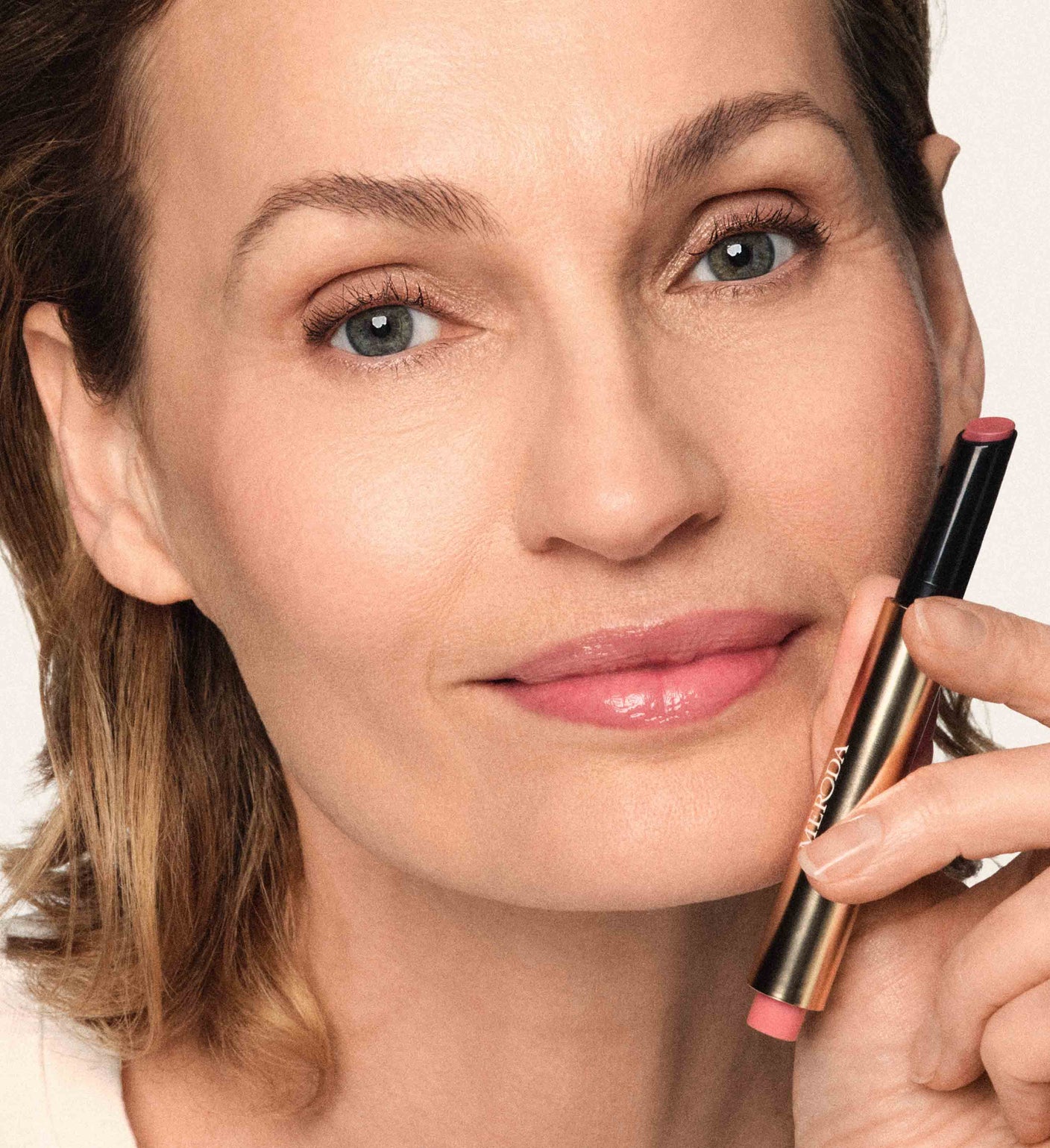Model wearing the Soft Touch Trio and holding the Hydrating Lip Tint in Dusty Rose for a natural, radiant look.