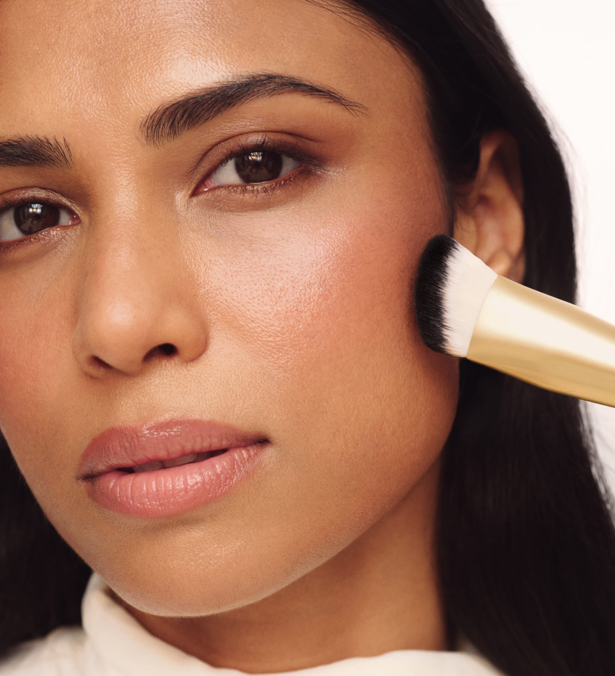 Model blending makeup on her cheek with Meroda Cosmetics The Essential Brush for a seamless, airbrushed finish.