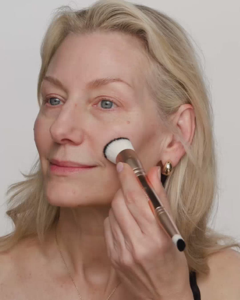 Mature woman blending Changing Foundation with a 2-in-1 brush to reveal its color-adapting finish.